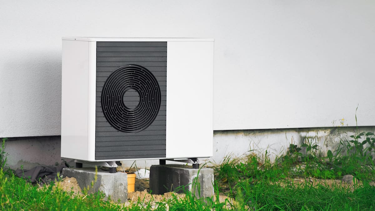 Een warmtepomp is op een stevige ondergrond tegen de gevel geplaatst.